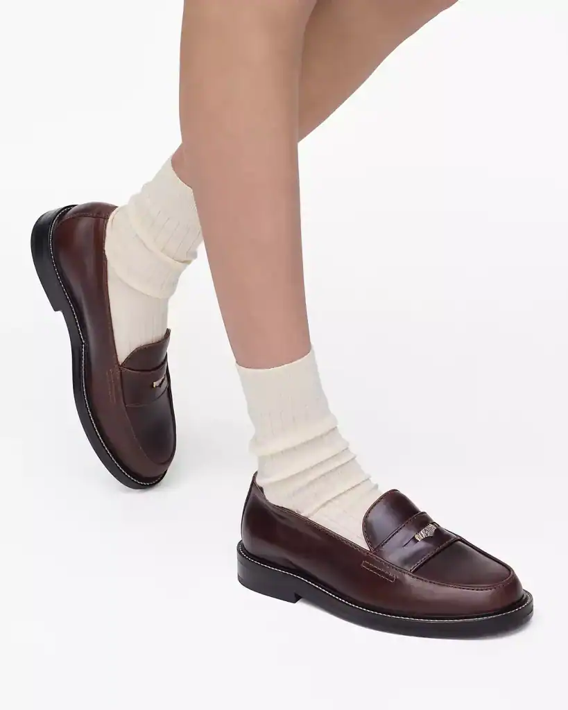 Chaussures mocassins en cuir marron avec semelle noire, portées avec des chaussettes crème épaisses, look élégant et classique pour homme ou femme.