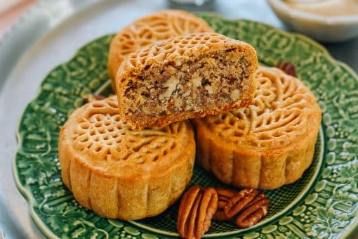 Galettes de mooncake et noix de pécan sur une assiette verte décorative, gâteau chinois traditionnel avec garniture de noix, pâtisserie sucrée asiatique, dessert pour célébrations, recette artisanale.