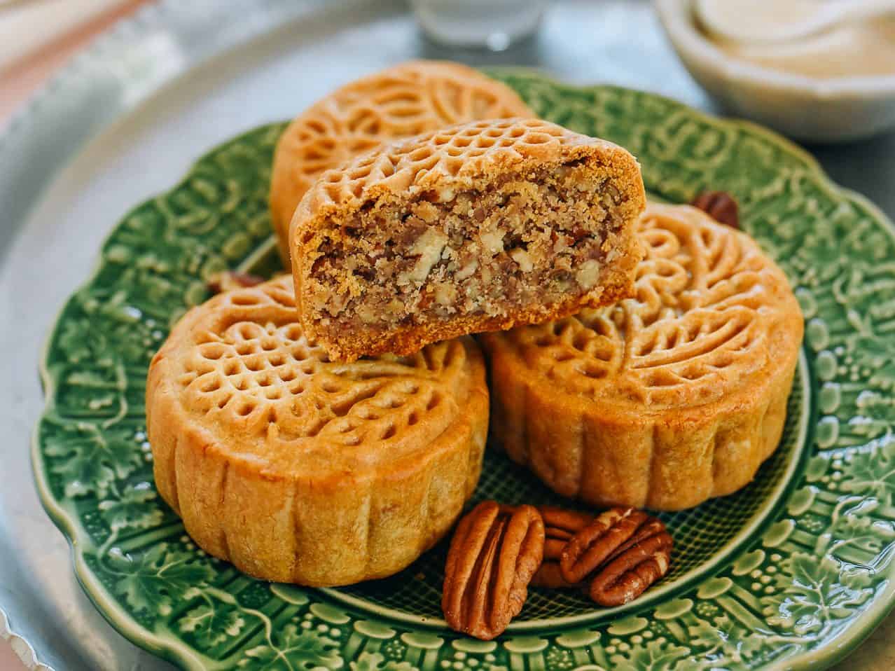 Galettes de mooncake et noix de pécan sur une assiette verte décorative, gâteau chinois traditionnel avec garniture de noix, pâtisserie sucrée asiatique, dessert pour célébrations, recette artisanale.