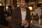 Un jeune homme porte un cardigan en laine sur un débardeur blanc dans un café parisien.