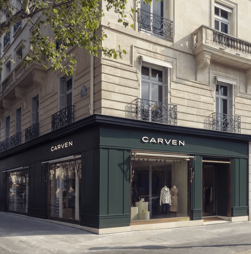 Façade de la boutique Carven installée au rez-de-chaussée d’un immeuble en pierre, sous un feuillage vert.