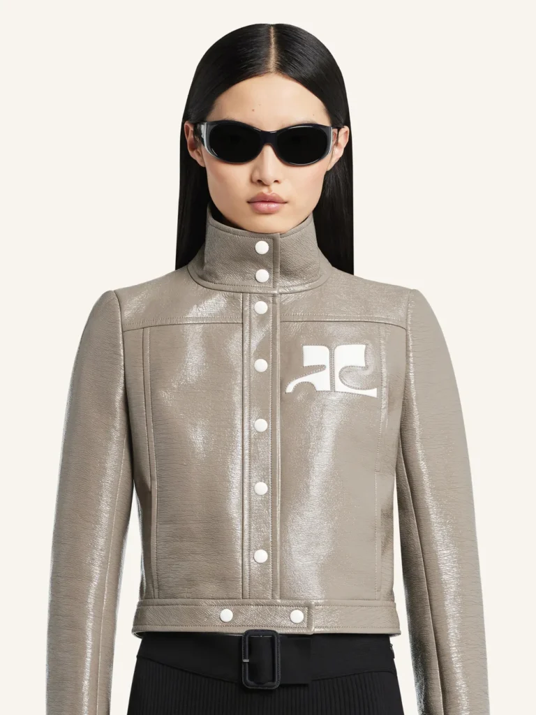 Mannequin en veste Courrèges grise brillante à col montant, boutons blancs et logo sur la poitrine