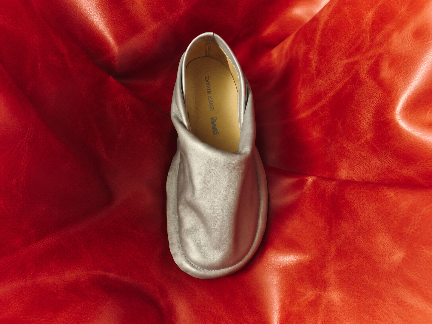 Chaussure Peu Form argentée de Camper et Issey Miyake sur un fond rouge plissé au format horizontal