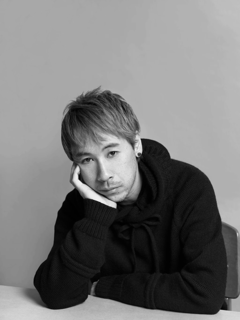 Jun Takahashi, fondateur d’Undercover, assis en pull noir dans un portrait en noir et blanc