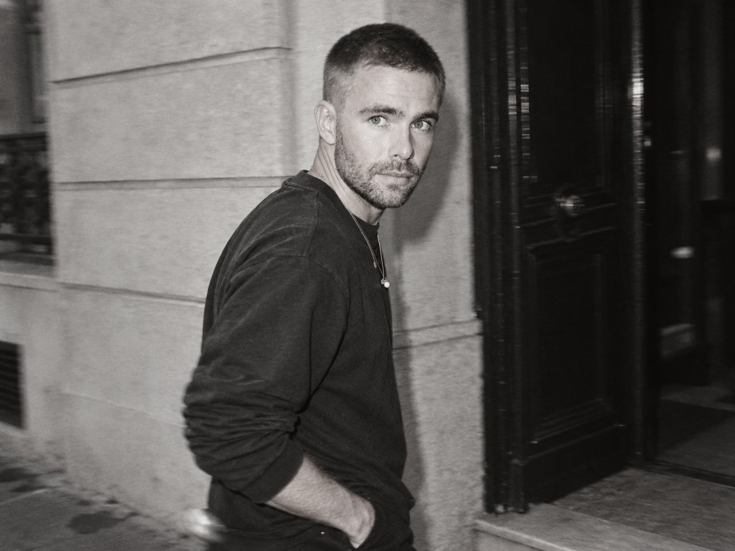 Kai Nesselrath marche devant une façade sombre, vêtu d’un sweat noir, dans un portrait en noir et blanc.