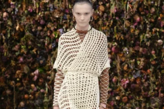 Look Maison Margiela printemps-été 2027 en robe filet écrue et résille sur un podium au décor floral