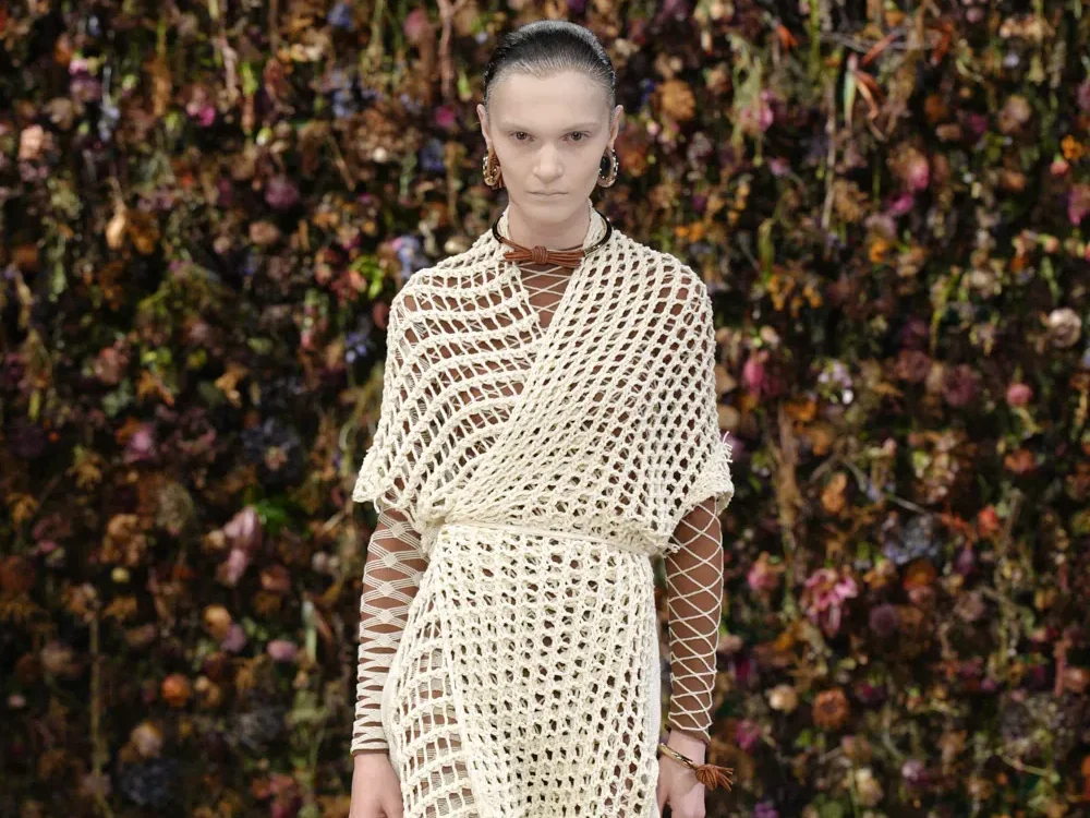 Look Maison Margiela printemps-été 2027 en robe filet écrue et résille sur un podium au décor floral