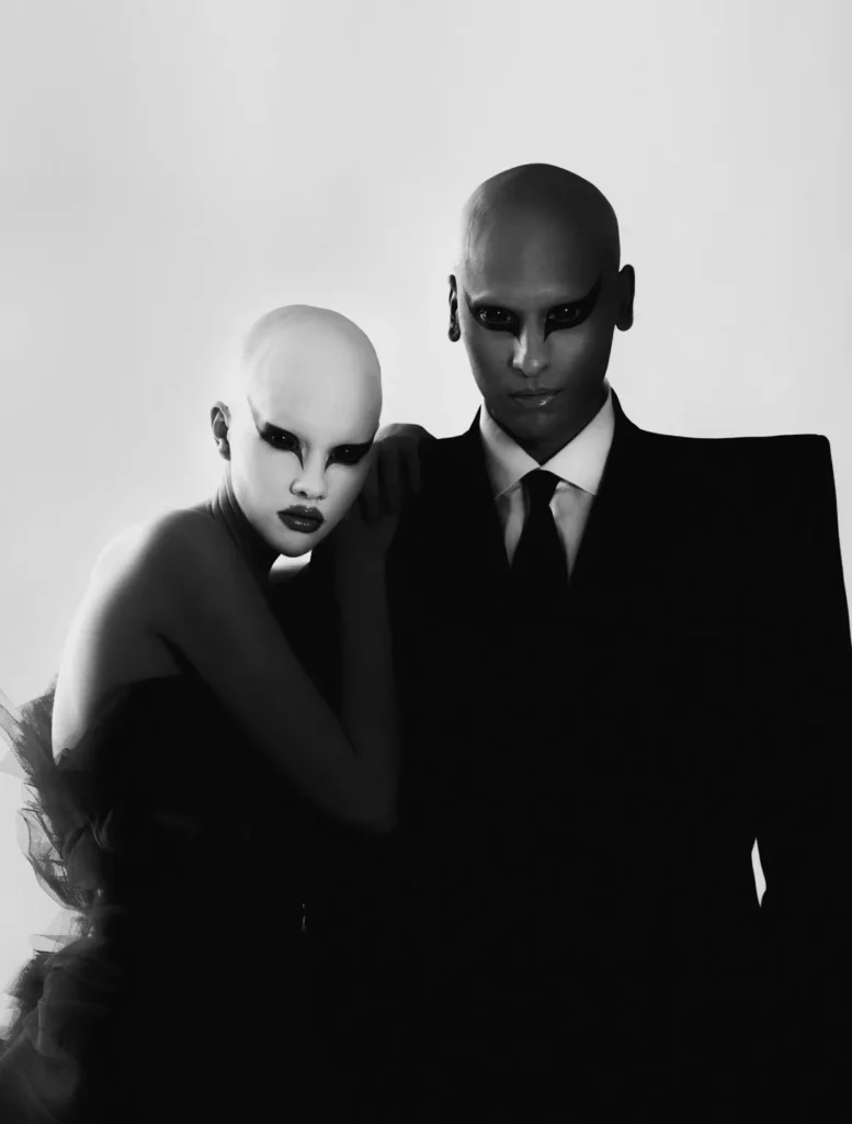 Hannah Rose Dalton et Steven Raj Bhaskaran maquillage noir graphique posent en noir et blanc, en tenue de tulle, l’autre en costume
