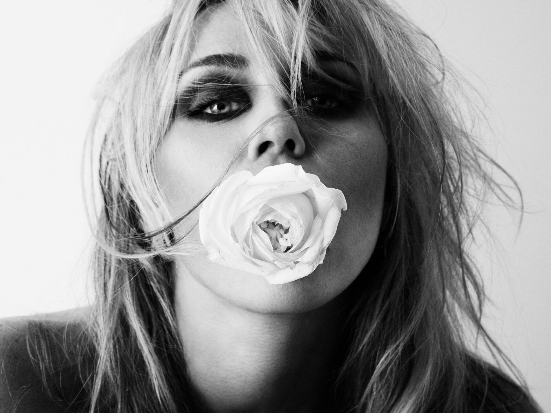 Portrait en noir et blanc de Miley Cyrus, les yeux maquillés de sombre et une rose blanche devant la bouche.