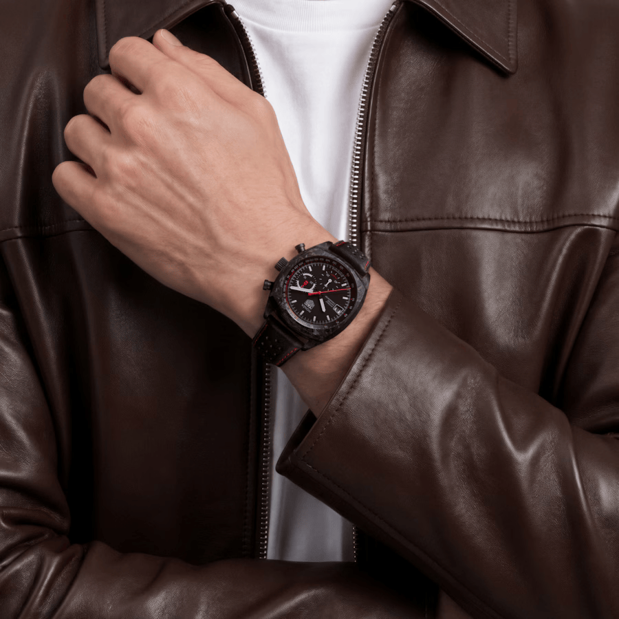TAG Heuer Monza Flyback Chronograph portée au poignet avec un blouson en cuir marron et un tee-shirt blanc.