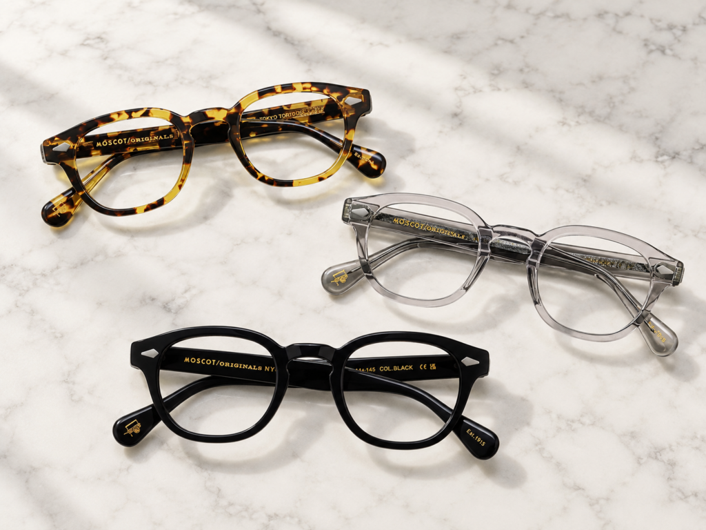 Trois lunettes Moscot Lemtosh, écaille, transparentes et noires, posées sur du marbre blanc.