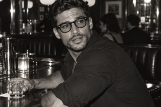 Homme portant une monture noire de style Moscot Lemtosh, assis au comptoir d’un bar Titre : Moscot Lemtosh, lunettes de vue noires