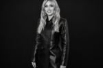 Miley Cyrus en manteau de cuir noir, photographiée en noir et blanc sur un fond noir