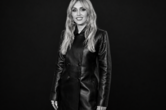 Miley Cyrus en manteau de cuir noir, photographiée en noir et blanc sur un fond noir