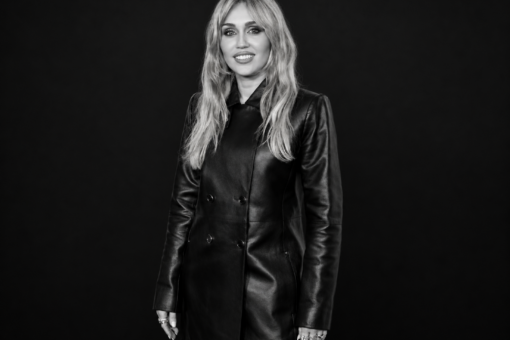 Miley Cyrus en manteau de cuir noir, photographiée en noir et blanc sur un fond noir