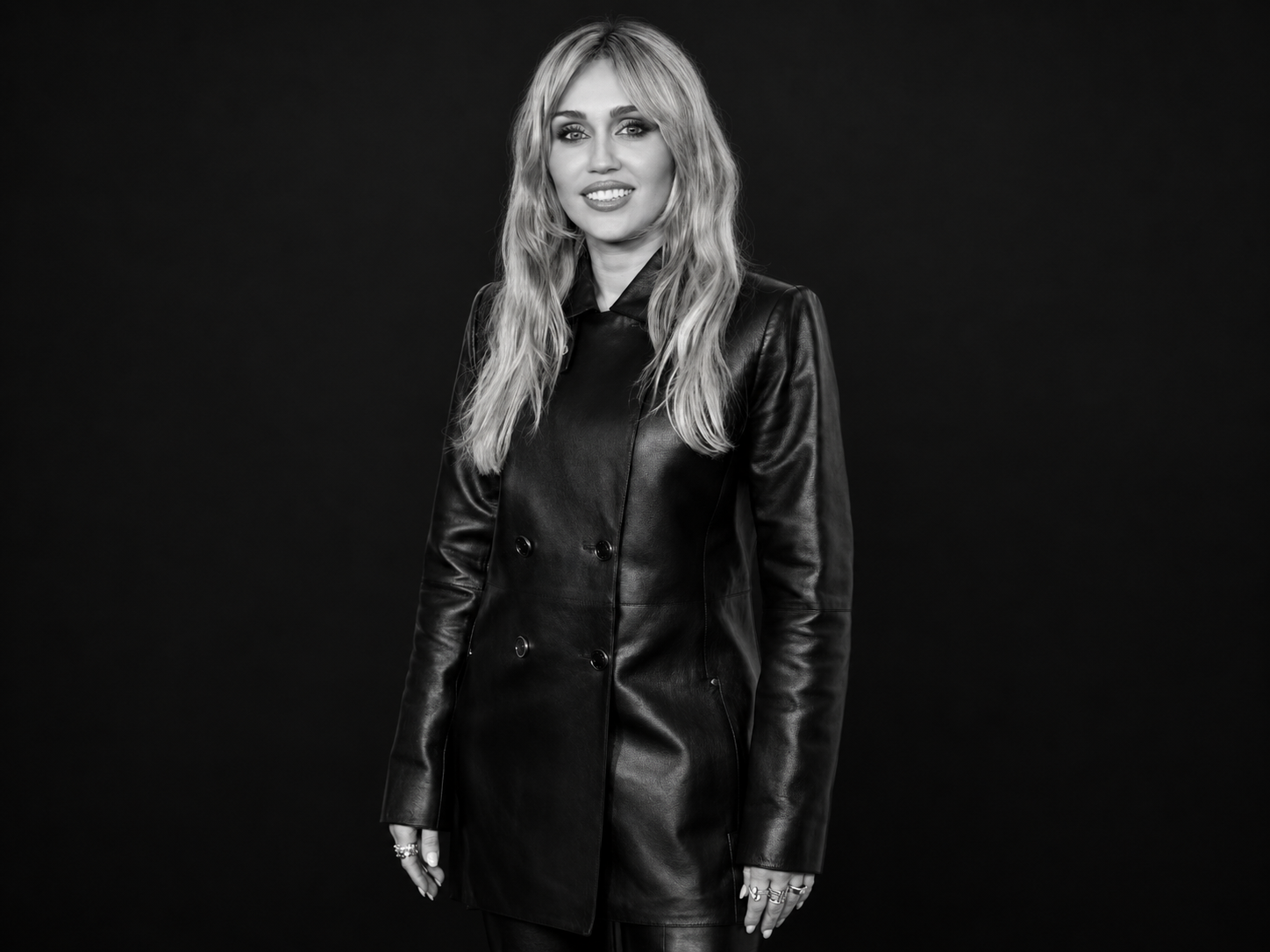 Miley Cyrus en manteau de cuir noir, photographiée en noir et blanc sur un fond noir