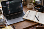 Ordinateur ouvert sur une playlist musicale à côté d’un carnet de sélection annoté et d’un casque audio.