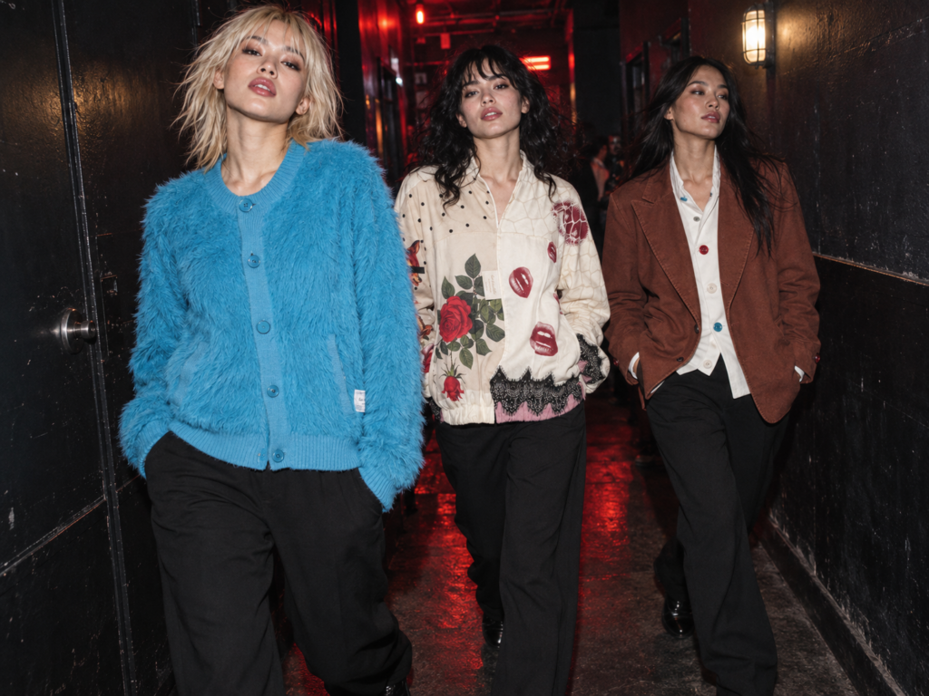 Trois jeunes femmes portent des vêtements Undercover et des pantalons noirs dans le couloir sombre d’un club.