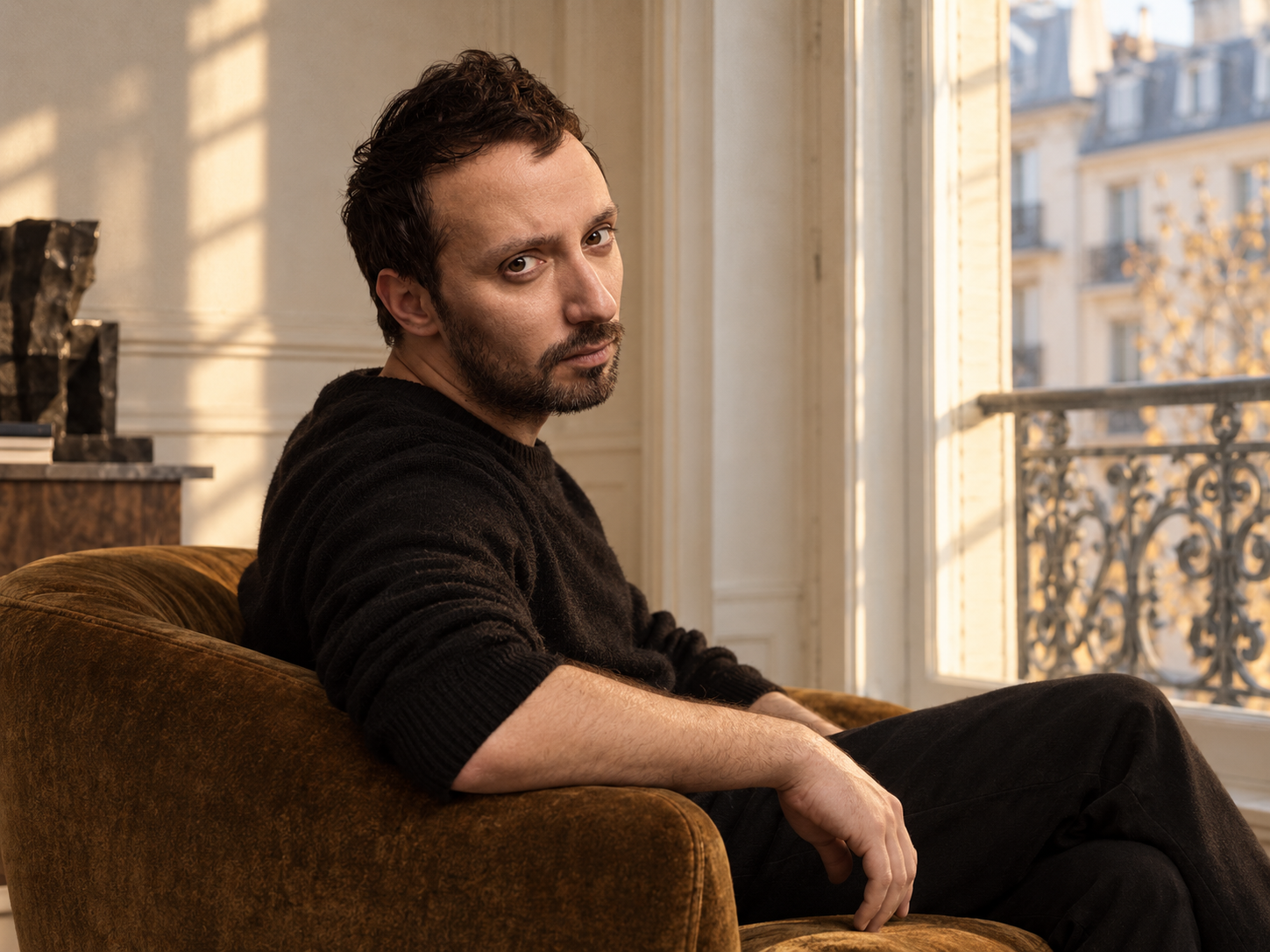 Portrait d’Anthony Vaccarello assis près d’une fenêtre, vêtu de noir.