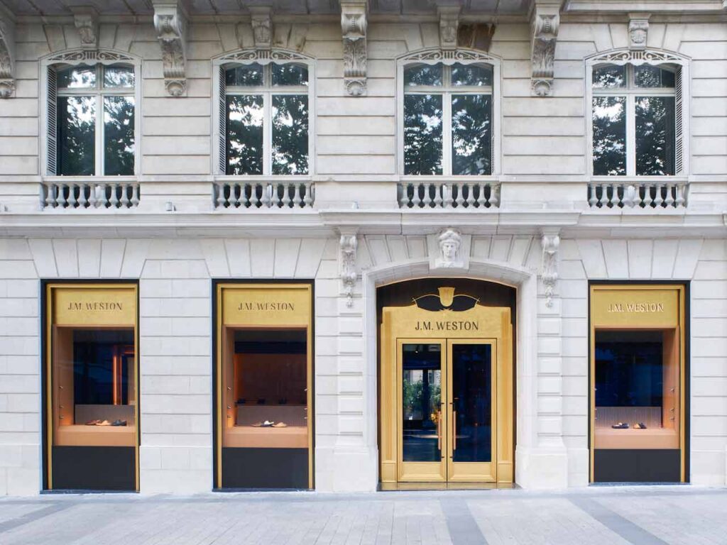 Façade de la boutique J.M. Weston sur les Champs-Élysées à Paris, avec son entrée dorée et trois vitrines de chaussures.