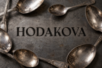 Logo HODAKOVA gravé en noir sur une plaque de fer, entouré de cuillères en argent