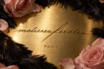 Logo Matières Fécales gravé sur une surface dorée, entouré de plumes noires et de roses rose pâle.
