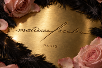 Logo Matières Fécales gravé sur une surface dorée, entouré de plumes noires et de roses rose pâle.
