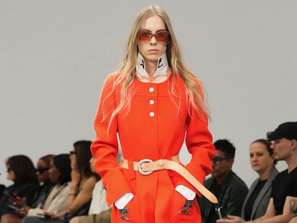 Silhouette Courrèges en manteau orange ceinturé, col montant blanc et lunettes rouges lors du défilé à Paris