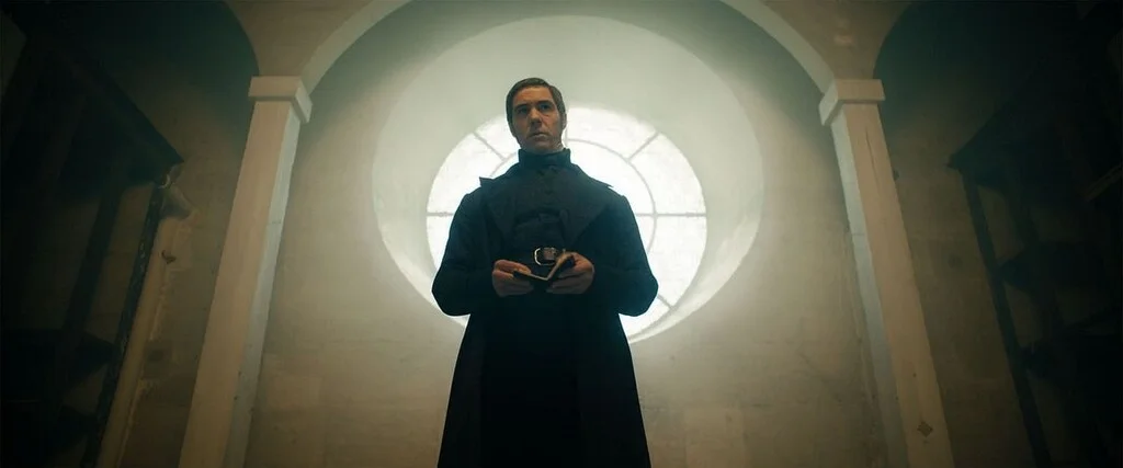 Javert, interprété par Tahar Rahim dans Les Misérables, porte un long uniforme noir devant une fenêtre circulaire.