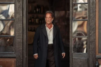 Jean Valjean, joué par Vincent Lindon dans Les Misérables, porte un long manteau noir et une chemise blanche.