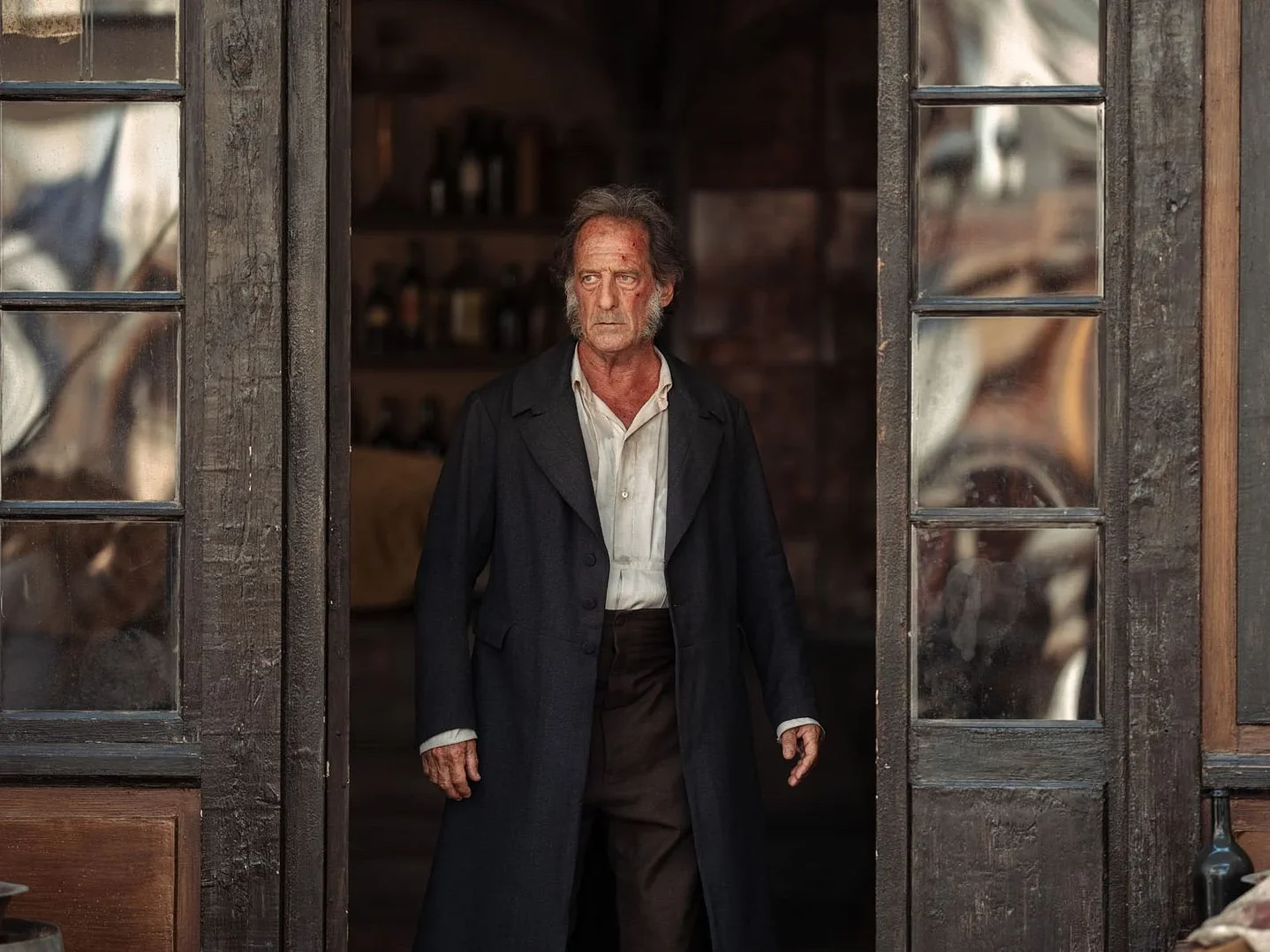 Jean Valjean, joué par Vincent Lindon dans Les Misérables, porte un long manteau noir et une chemise blanche.