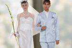 Deux mannequins en tenues de mariés au défilé agnès b. printemps-été 2027 à Paris : robe blanche avec voile et fleur, costume bleu ciel à double boutonnage.