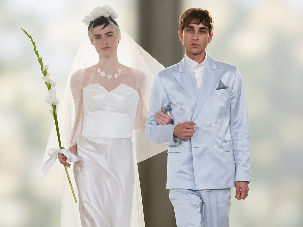Deux mannequins en tenues de mariés au défilé agnès b. printemps-été 2027 à Paris : robe blanche avec voile et fleur, costume bleu ciel à double boutonnage.