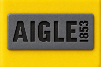 Logo Aigle 1853 gravé sur une plaque de caoutchouc gris fixée sur une surface en caoutchouc jaune.