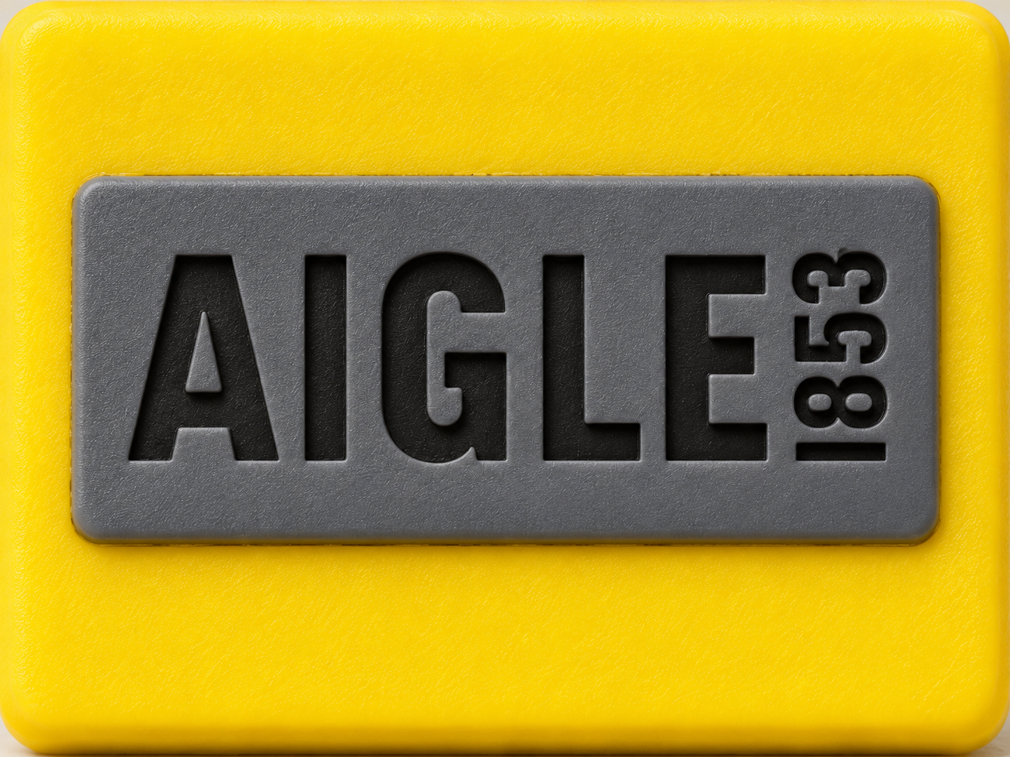 Logo Aigle 1853 gravé sur une plaque de caoutchouc gris fixée sur une surface en caoutchouc jaune.