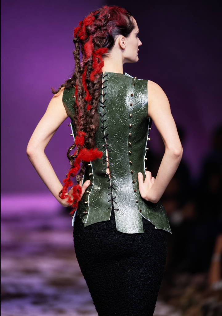 Mannequin de dos portant un corset vert à lacets et une coiffure tressée rouge et noire lors du défilé Highland Rape d’Alexander McQueen en 1995.