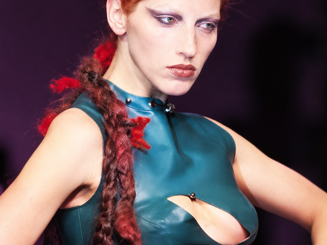 Mannequin aux cheveux roux tressés portant un haut en cuir vert découpé lors du défilé Highland Rape d’Alexander McQueen en 1995.