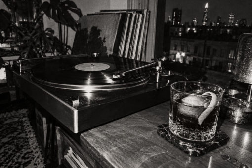 Cocktail The Darkroom dans un verre bas à côté d’une platine vinyle, dans un appartement londonien photographié en noir et blanc.