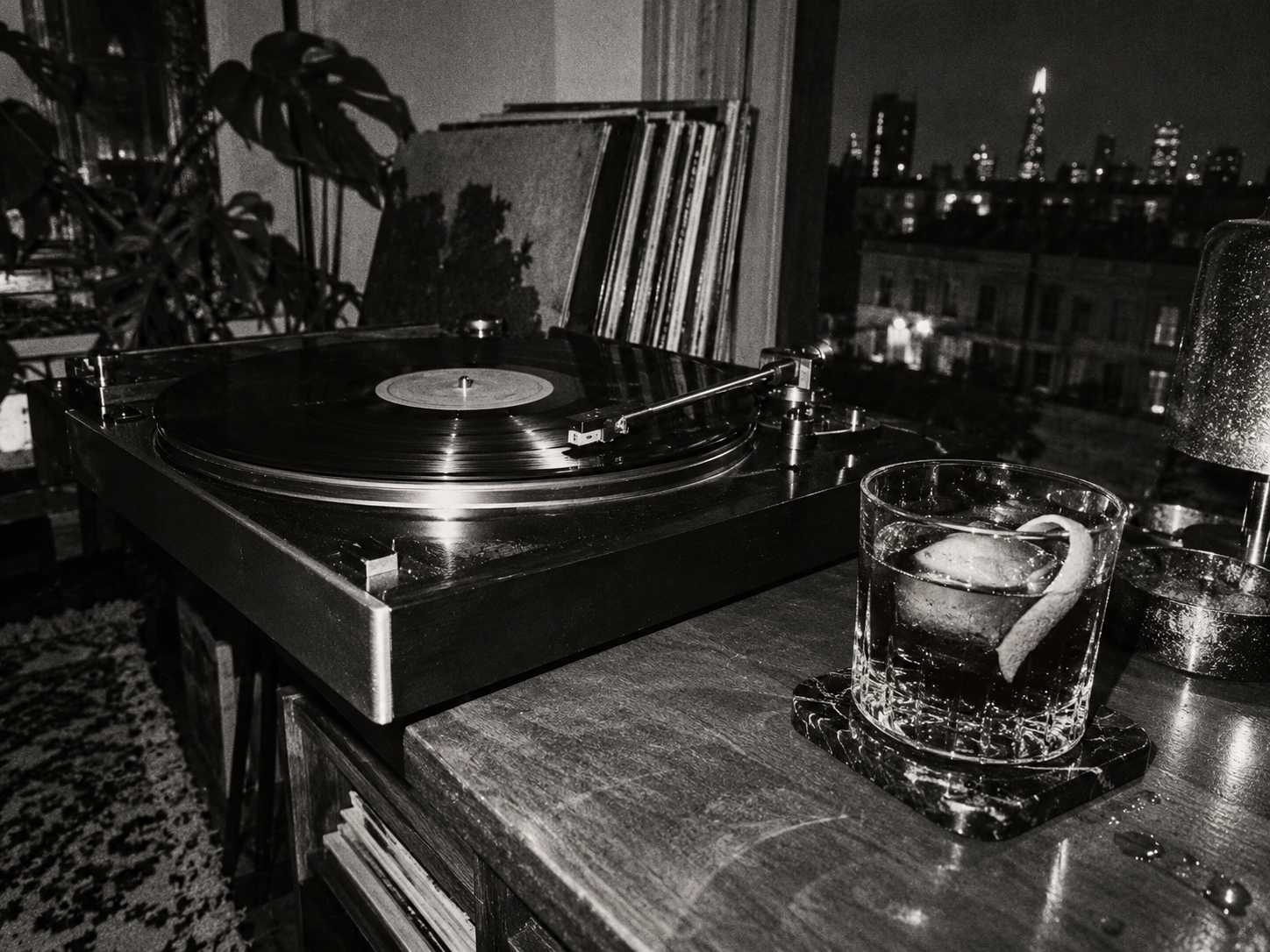 Cocktail The Darkroom dans un verre bas à côté d’une platine vinyle, dans un appartement londonien photographié en noir et blanc.