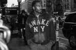 Homme portant un sweat à capuche zippé Awake NY dans une rue de New York, photographié dans un style paparazzi noir et blanc argentique.