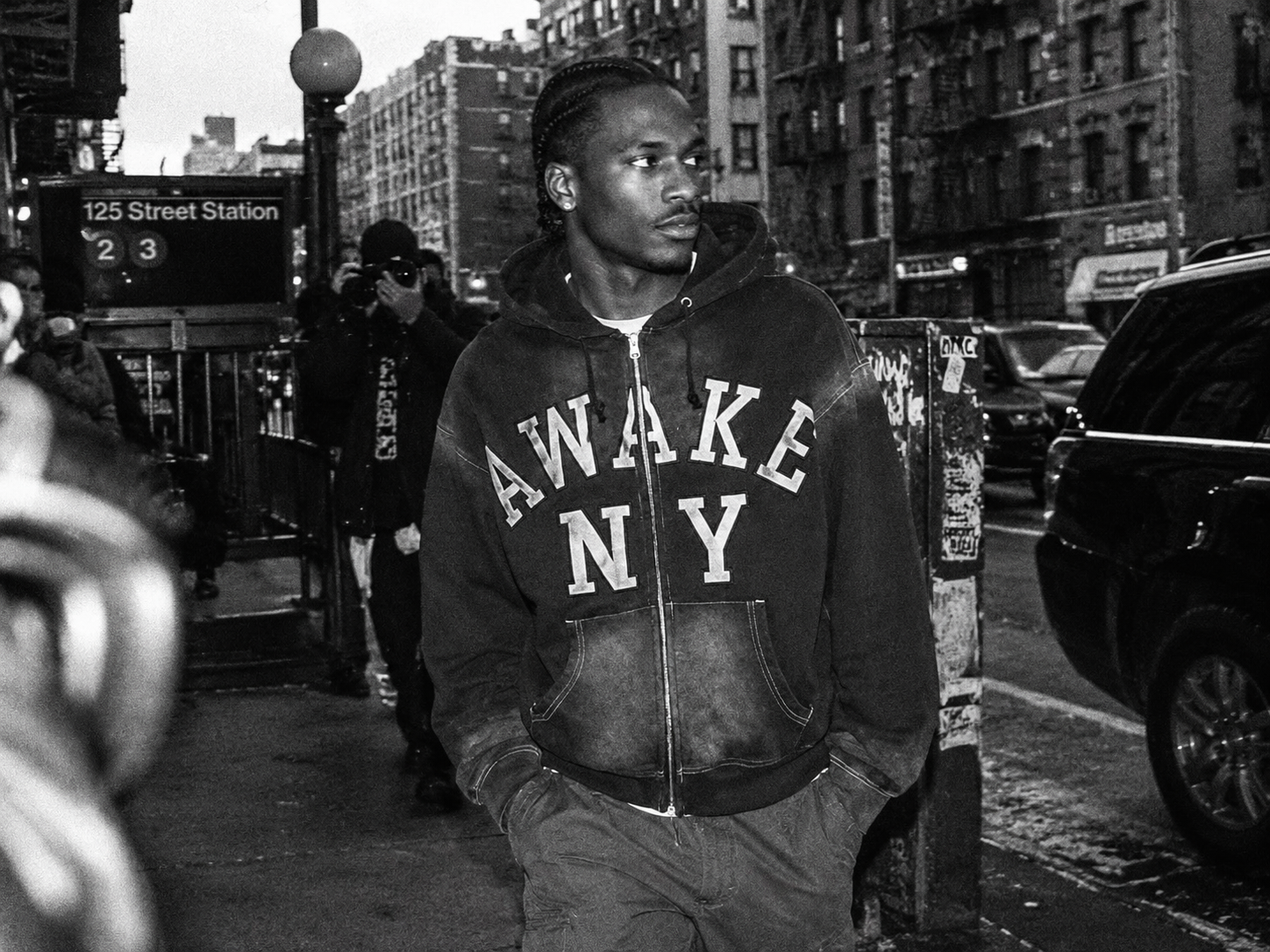 Homme portant un sweat à capuche zippé Awake NY dans une rue de New York, photographié dans un style paparazzi noir et blanc argentique.