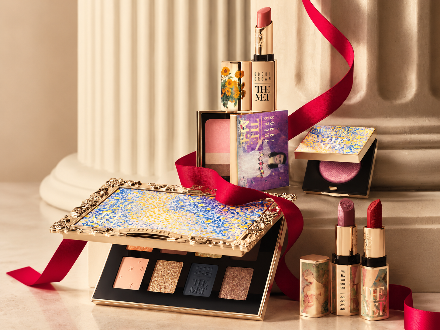 Collection Bobbi Brown x The Met avec palette de huit fards, rouges à lèvres et poudres dans des boîtiers ornés d'œuvres d'art, entourés d'un ruban rouge.