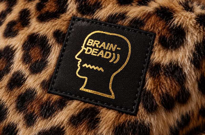 Logo Brain Dead imprimé en doré sur une étiquette noire cousue sur un tissu en fausse fourrure léopard.