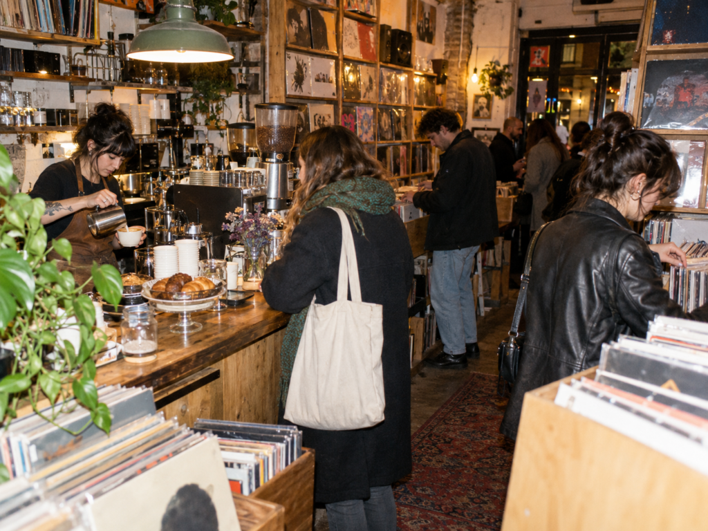 Dans un café-disquaire, une barista prépare un café pendant que des clients parcourent les bacs de vinyles.