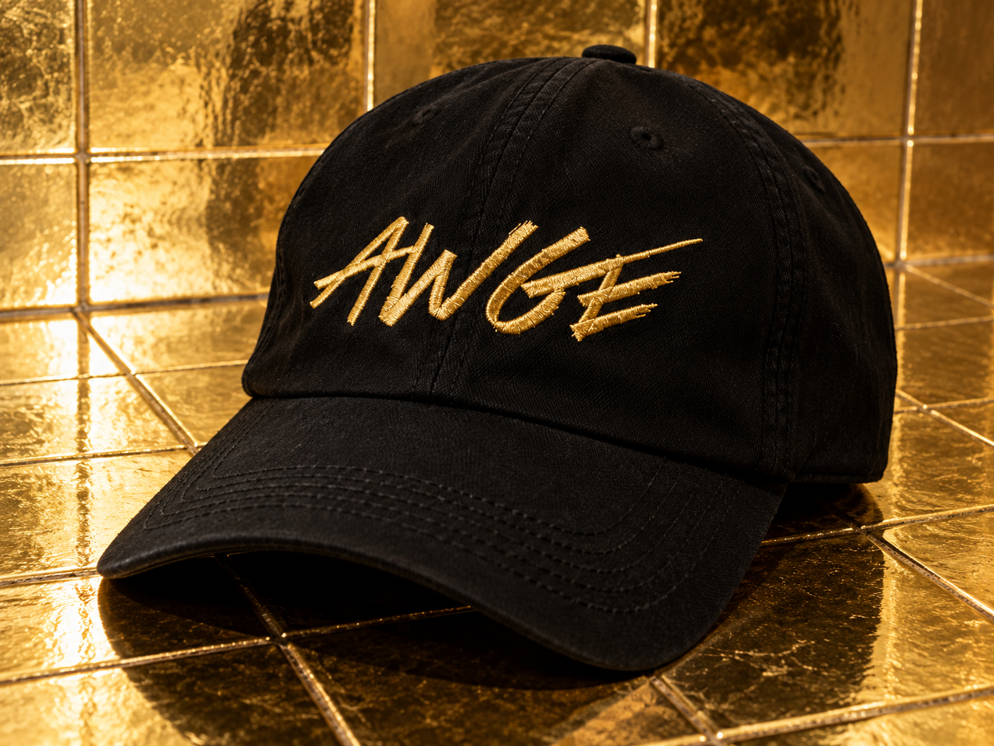 Casquette noire AWGE avec logo brodé en doré, posée sur un carrelage doré brillant.