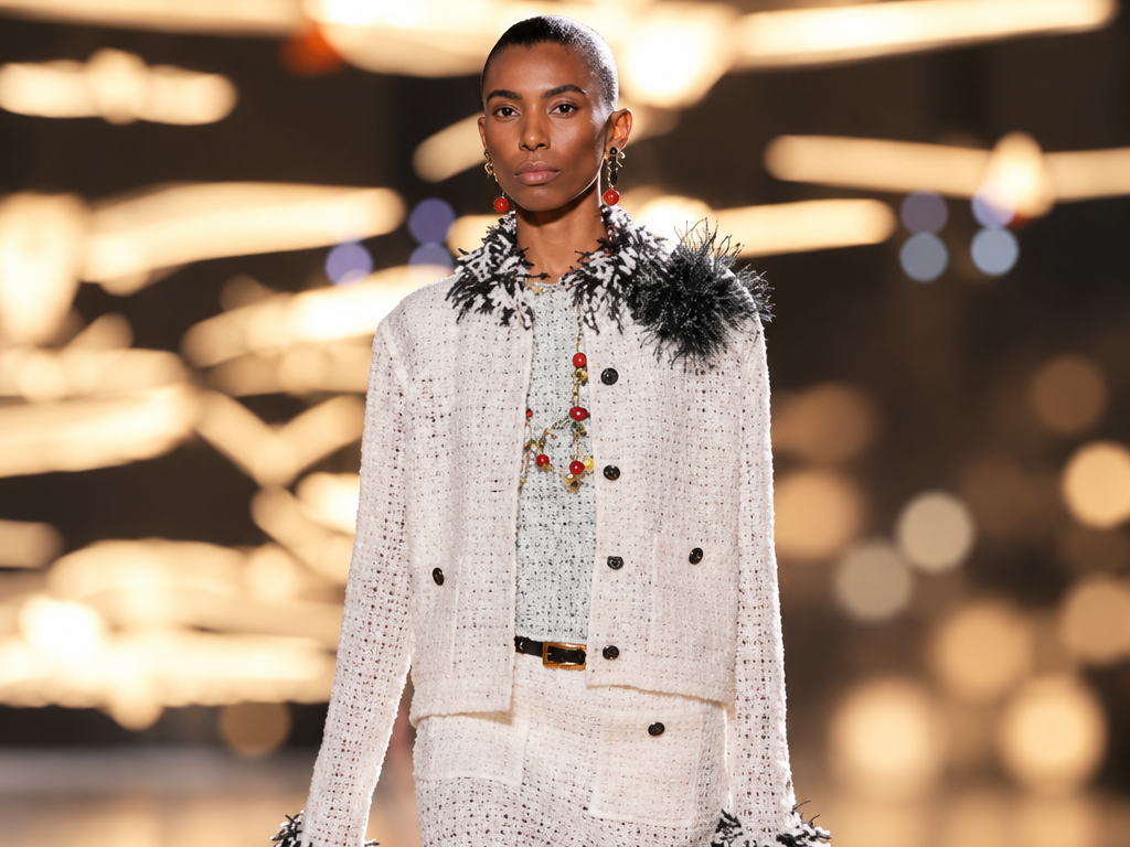 Mannequin portant un tailleur Chanel en tweed blanc à franges noires, composé d'une veste et d'une jupe assortie, lors du défilé printemps-été 2027 à Paris.