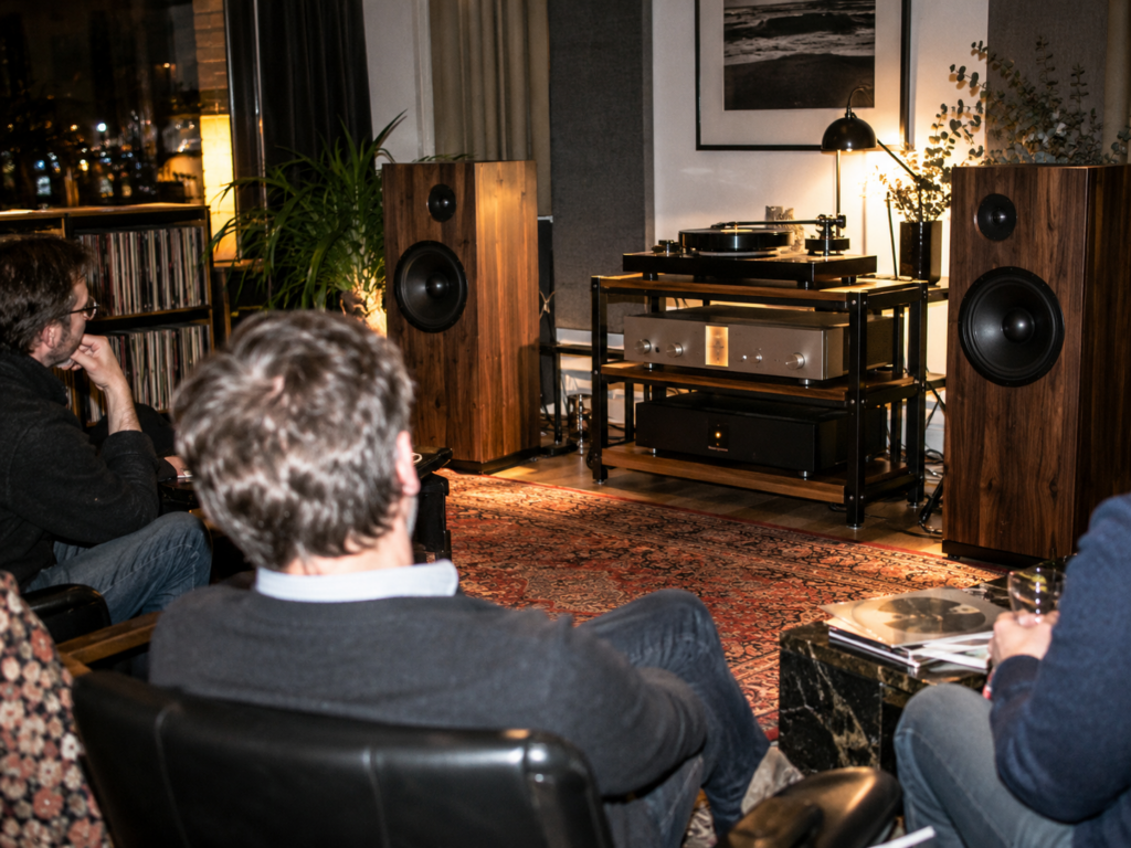 Clients dans un auditorium hi-fi écoutant un vinyle sur une platine entourée d'enceintes et d'amplificateurs.