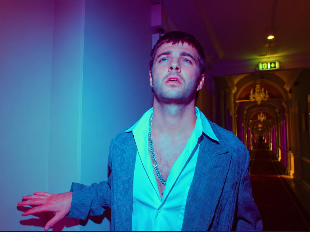 Grian Chatten, chanteur de Fontaines D.C., dans le clip Marianne, extrait de l'album Dopamine Chamber, sous des lumières bleues et violettes.