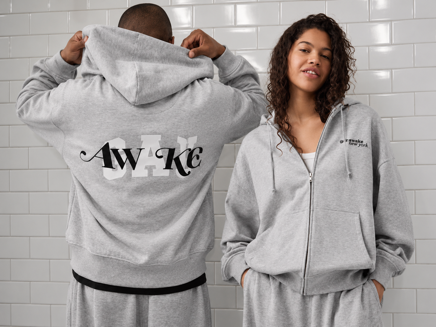 Deux mannequins portent des ensembles gris à capuche de la collaboration Gap x Awake NY, avec les logos des marques sur les vêtements.