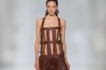 Mannequin portant une robe marron à lanières de cuir et ornements métalliques lors du défilé Jean Paul Gaultier printemps-été 2027 à Paris.
